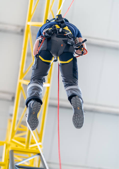 Trabajador suspendido con arnés junto a una torre amarilla